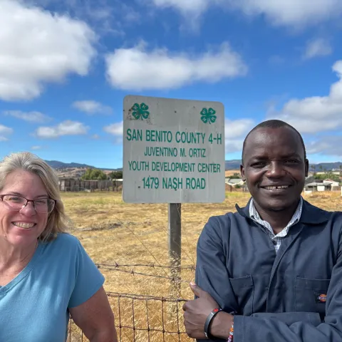 Julie Katawicz and Hedman Okella pose in front of a sign: San Benito County 4-H, Juventino M. Ortiz youth development center, 1479 Nash Road
