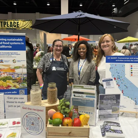 Three women stand by banner: Strengthening sustainable farming and food systems in California