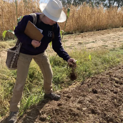 While holding a clipboard in her right hand, Margaret Lloyd grabs a handful of soil with her left hand from a tilled field.
