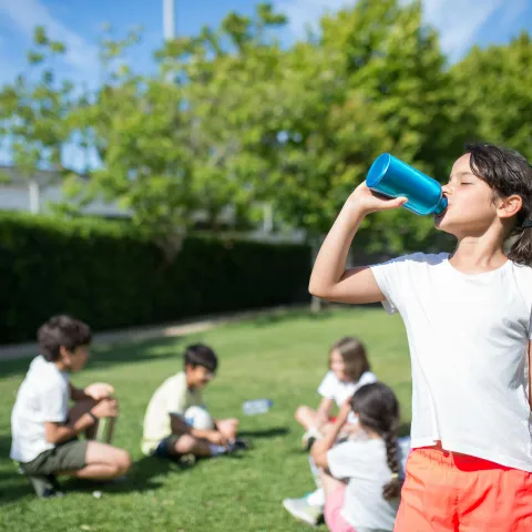 Group of children sitting on soccer field; one young girl drinks from a water bottle