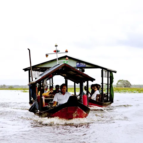 Man drives a boat pulling another boat containing passengers across the water