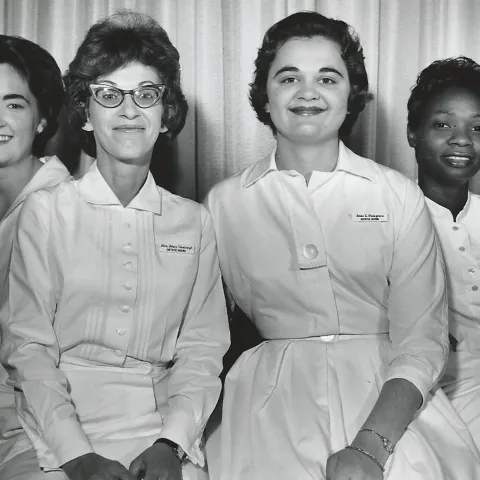Three White women and one Black woman wearing white uniforms pose in a black and white photo