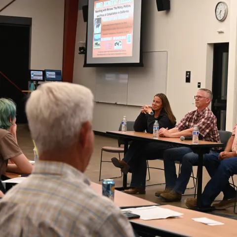 A woman and two men sit at a table facing an audience