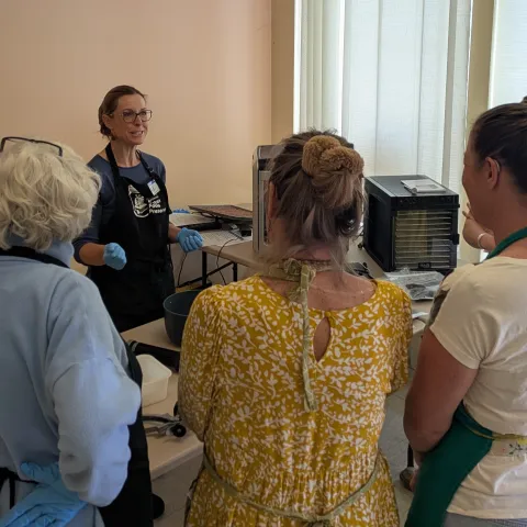 A group of adult watching another adult demonstrating jerky making.
