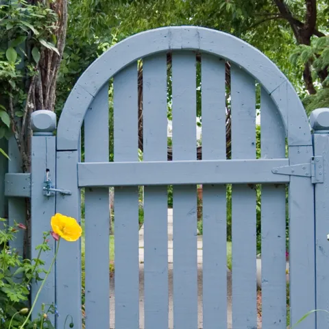 Gray arched garden gate and fence surrounded by plants