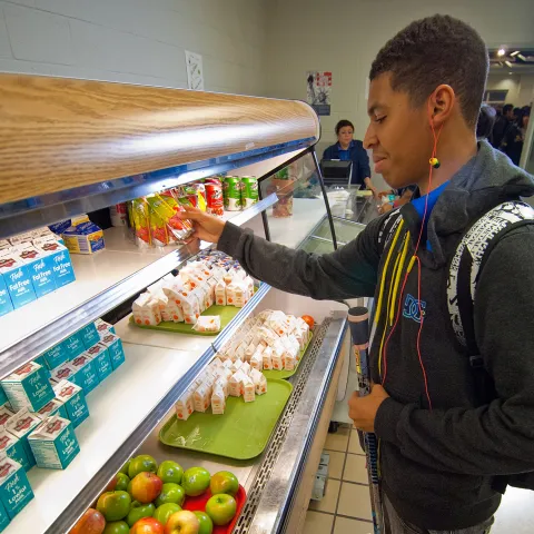 A high school student grabs a pre-made meal from the school cafeteria lunch line.