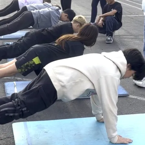 Six fifth-grade students do push ups at a school yard as part of fitness testing, while their peers look on