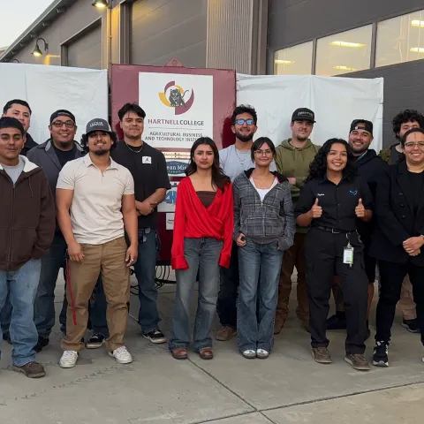 A farm robotics team stands in front of a backdrop that reads Hartnell College