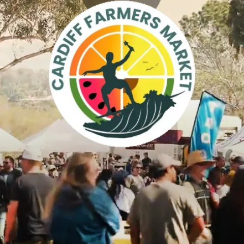 A farmers market amongst eucalyptus trees with rows of tents and shoppers, featuring a circular logo with "Cardiff Farmers Market" text, a surfer, and fruit.