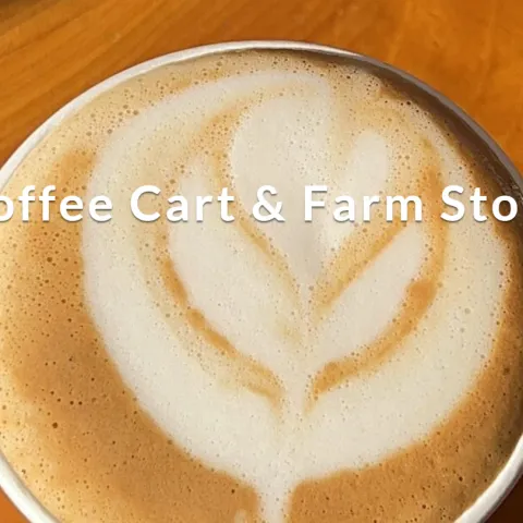 A close-up overhead view of a coffee drink with plant-shaped foam art. Its cup sits on a wooden surface. Text overlay reads "Coffee Cart & Farm Store."