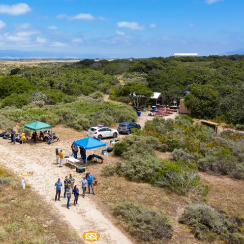 An aerial view of people standing under a tent in scrubland