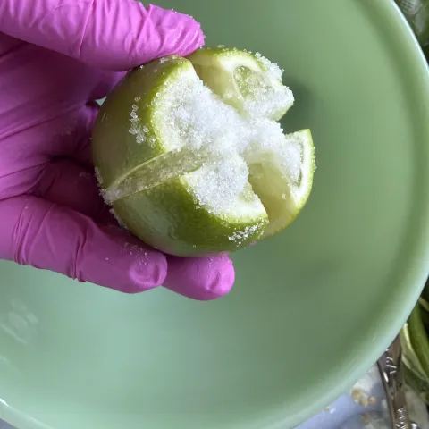  gloved hand holds a quartered lime covered in salt over a bowl