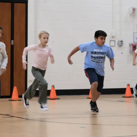 Image of four adolescents performing a school-based physical fitness test indoors. 