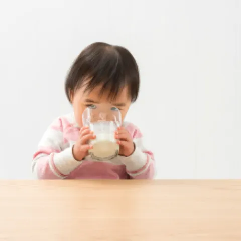 Small child wearing pink outfit holding glass with two hands drinking milk