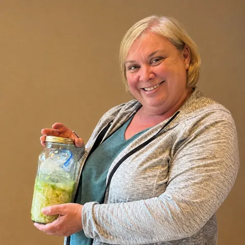 a smiling woman holding a half-gallon jar of homemade sauerkraut