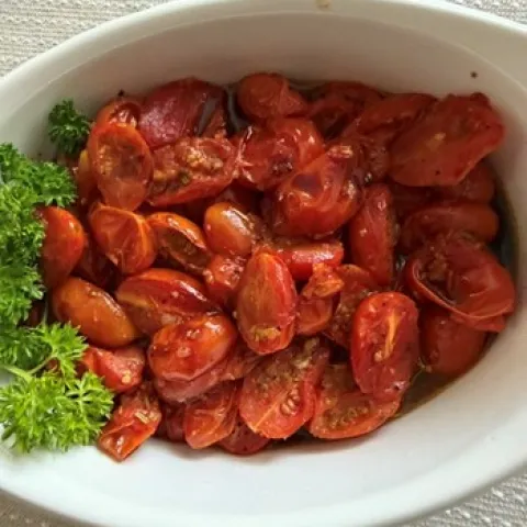 Roasted cherry tomatoes in a white bowl with a green garnish