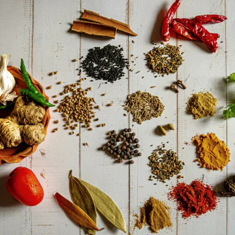 Small piles of various herbs and spices next to a bowl of whole turmeric, garlic, and peppers.