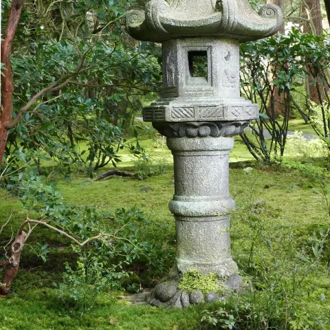 A beautiful Japanese lantern in a garden surrounded by moss and bushes.