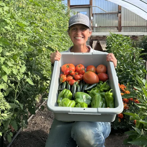 Leah Larsen of Bidwell Canyon Farm displays a container with a harvest of tomatoes and peppers from her hoophouse