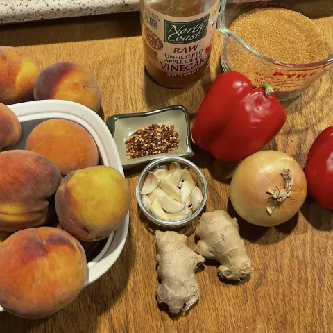 Peaches, garlic, peppers, onions, and ginger on a wood surface.