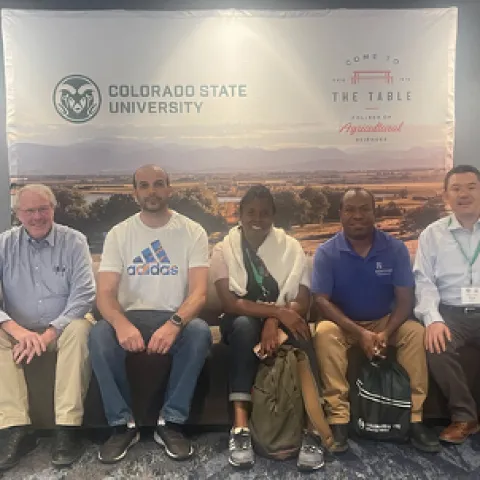 Five people sit on a bench in front of a Colorado State University banner