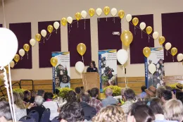 Seated audience, arch of balloons in yellow and white, UCCE banners.