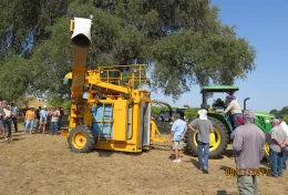 A group of farmers looking at a stationary mechanical grape harvester
