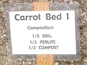 Wooden sign labeled "Carrot Bed 1" detailing its composition as 1/3 soil, 1/3 perlite, and 1/3 compost.