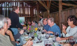A dozen people seated at a table eating dinner in a barn.