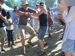 A man and woman contra dance while surrounding people clap.