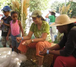 Two adults seated on hay bales with two standing children nearby.