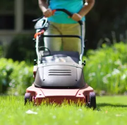 Hands pushing a lawn mower through green grass.