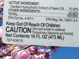 A product label detailing ingredients, safety instructions, and caution warnings, set against a backdrop of pink flowering branches.