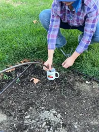 Advisor at the corner of an irrigation plot dipping the end of a drip tube into a cup of hot water to make it easier to insert a fitting.