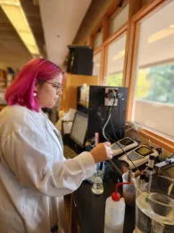 Woman in white lab coat places a probe into liquid in a beaker.