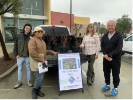 Four master gardener's stand in front a truck with trees in pots in its trunk