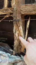 A finger poking a rotten, spongy wood beam.