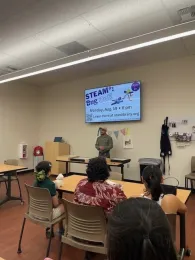 Smiling man in hat speaking to a group of people about bugs.