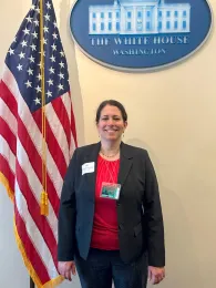 Ruth Dahlquist-Willard standing next to the American flag under a blue sign that reads