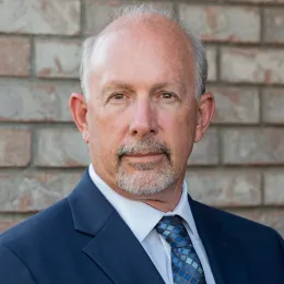A photo of Dave Green with a gray background, he is wearing a gray suit