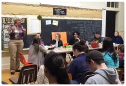 Youth sitting at tables with a 4-H adult volunteer addressing them