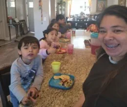 A mother smiling at the camera with four children eating a snack in the background