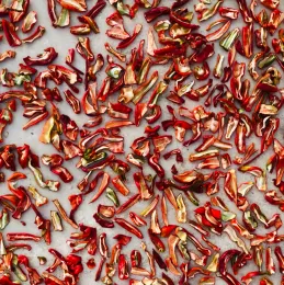 Sliced red peppers dehydrated on parchment paper. 