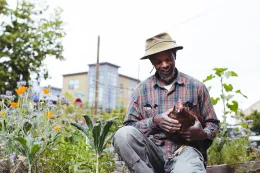 Community gardener holding chicken near raised beds full of crops