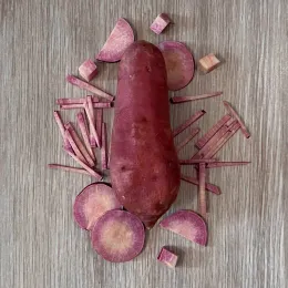 A whole purple-skinned sweet potato with pieces of its light purple flesh around it