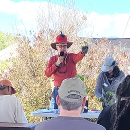Person addressing audience seated at picnic tables