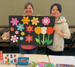 two women volunteers hold up a colorful paper flower collage