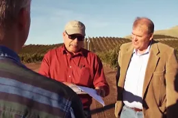 two men look at a clipboard, presenting audit results to a farmer