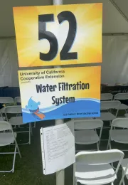 Sign showing “Water Filtration System” with booth number displayed at the UC Cooperative Extension station.