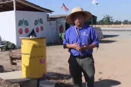 A man stands in front of a jug of water, presenting about handwashing standards